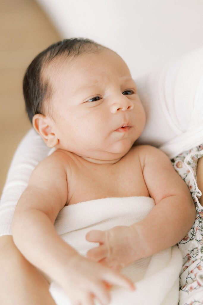 Awake newborn baby wrapped in a soft blanket during a natural studio newborn session.