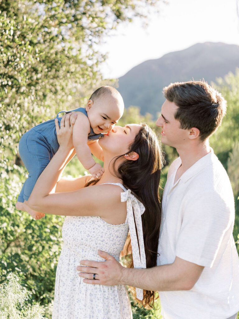 Mom kissing her baby while dad looks on during natural family photos with kids in Santa Clarita