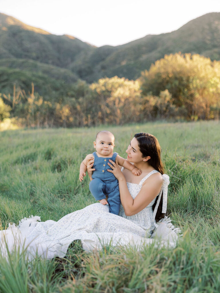 Mom holding her baby while sitting on the blanket outdoors during a natural family session