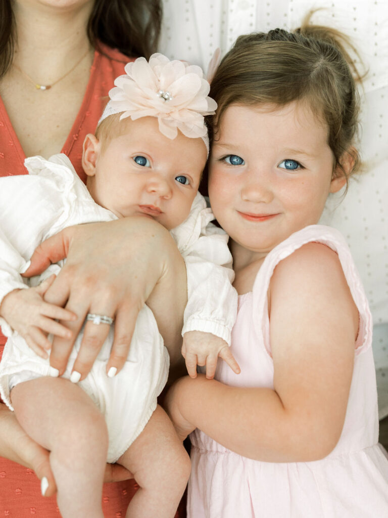 Newborn baby girl cuddled beside her older sister during a soft lifestyle newborn session.