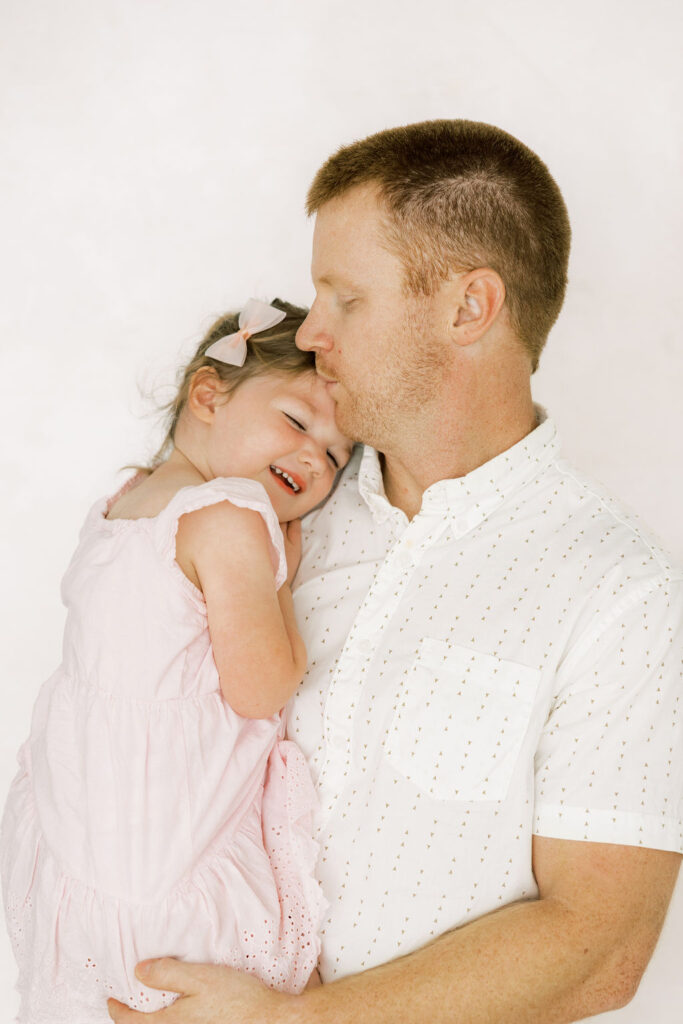 Dad kissing his older daughter during a sweet family moment at their newborn session.
