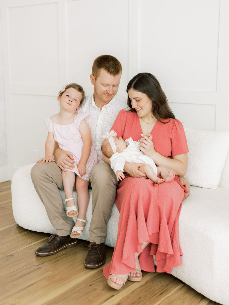 Family of four relaxing together on a white sofa during newborn photos in Santa Clarita.
