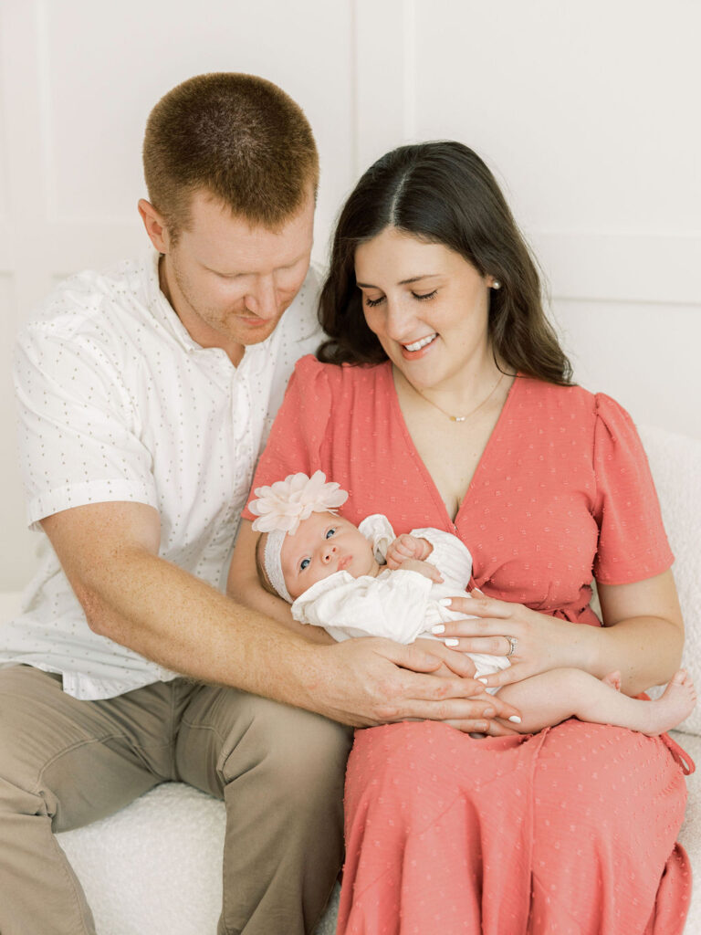 Mom and dad sitting together and looking down at their newborn baby girl during newborn photos in Santa Clarita.