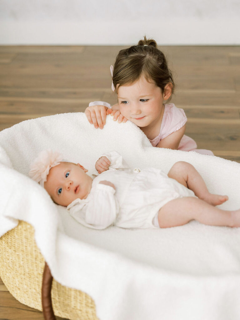Older sister leaning over her newborn baby sister during a relaxed Santa Clarita newborn photography session.