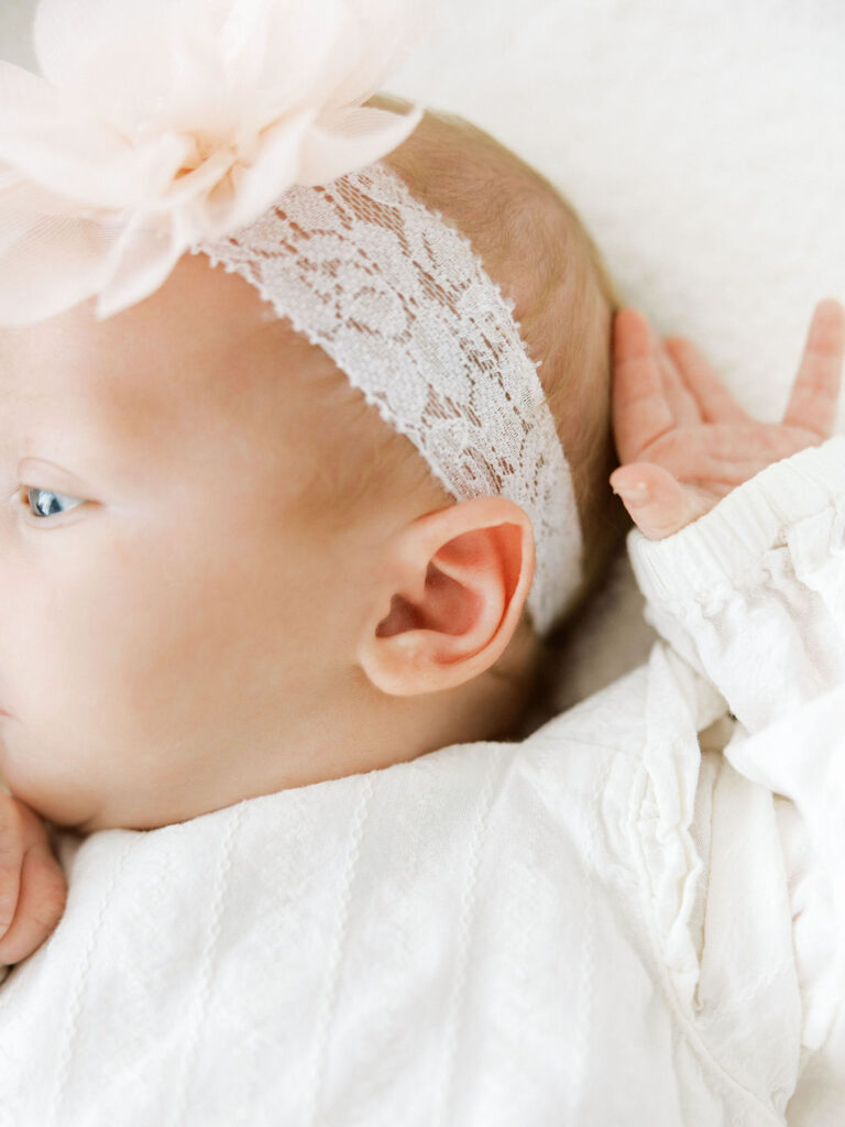 Close detail of a newborn baby girl wearing a delicate lace floral headband and white outfit.