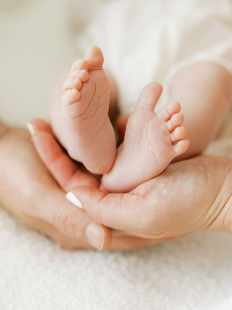 Close up of a newborn baby’s tiny feet resting in a parent’s hands during a lifestyle newborn session.