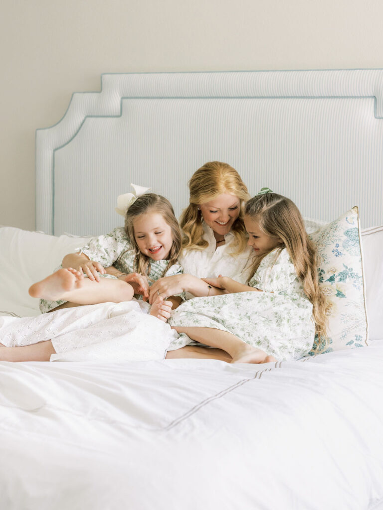 Mom relaxing on a bed with her two older daughters as they gather around and cuddle their newborn sibling during a natural Santa Clarita newborn session.