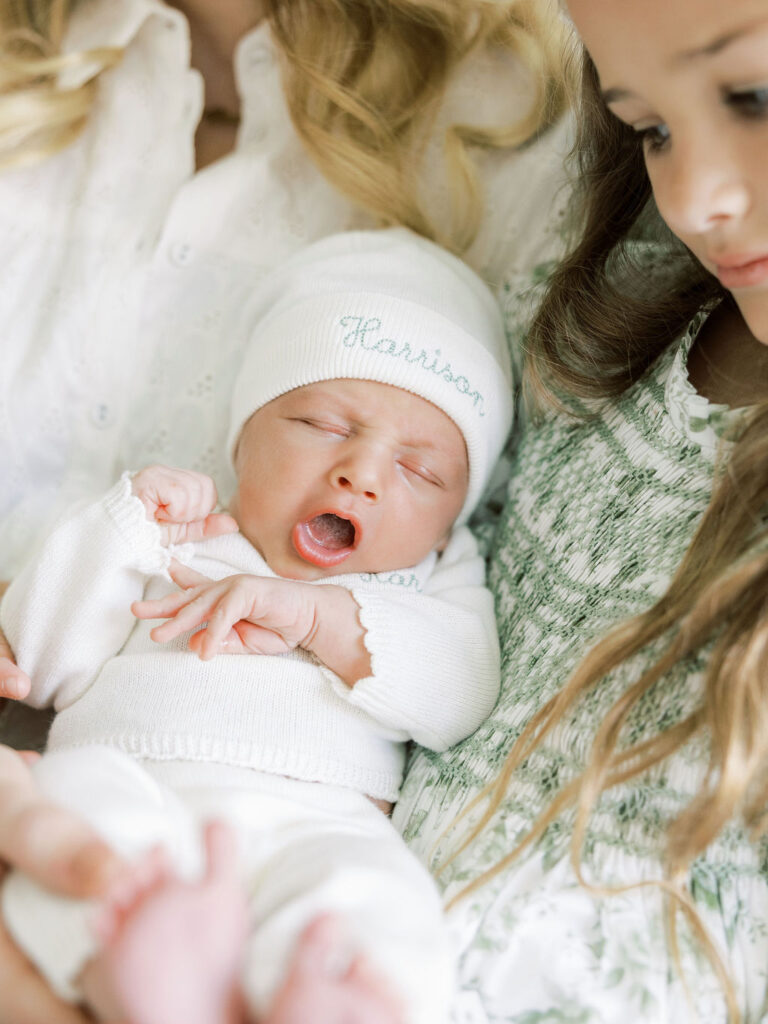 Newborn baby in a white knit outfit resting beside an older sister during a natural newborn photos with siblings session.