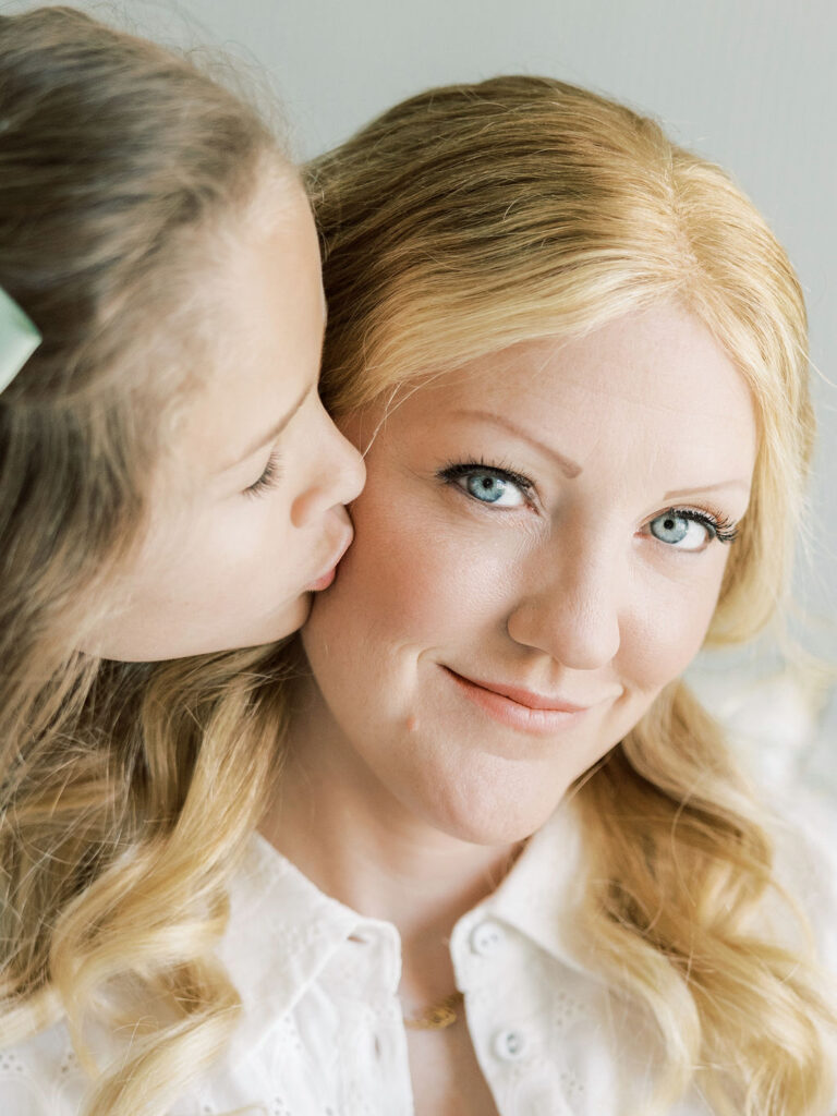 Older daughter giving mom a kiss during a sweet family moment at a newborn photos with siblings session.