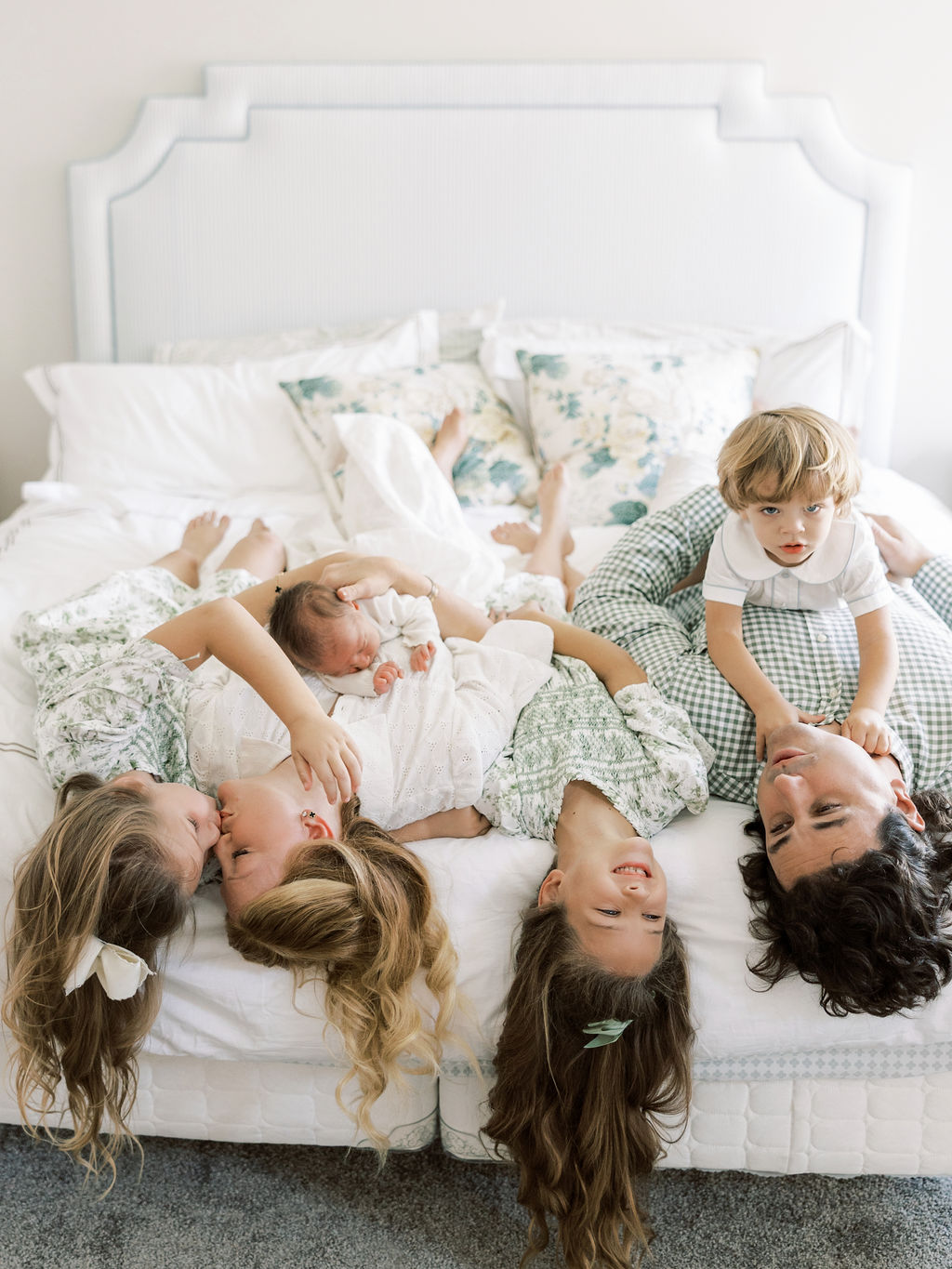 Family of six lying together on a bed with three older siblings gathered around their newborn baby during newborn photos with siblings in Santa Clarita.