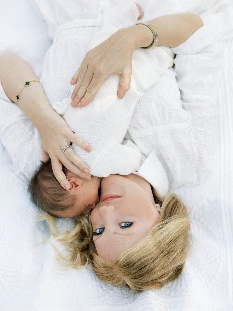 Mom lying on a bed while cuddling her newborn baby during a soft, natural Santa Clarita newborn photography session.