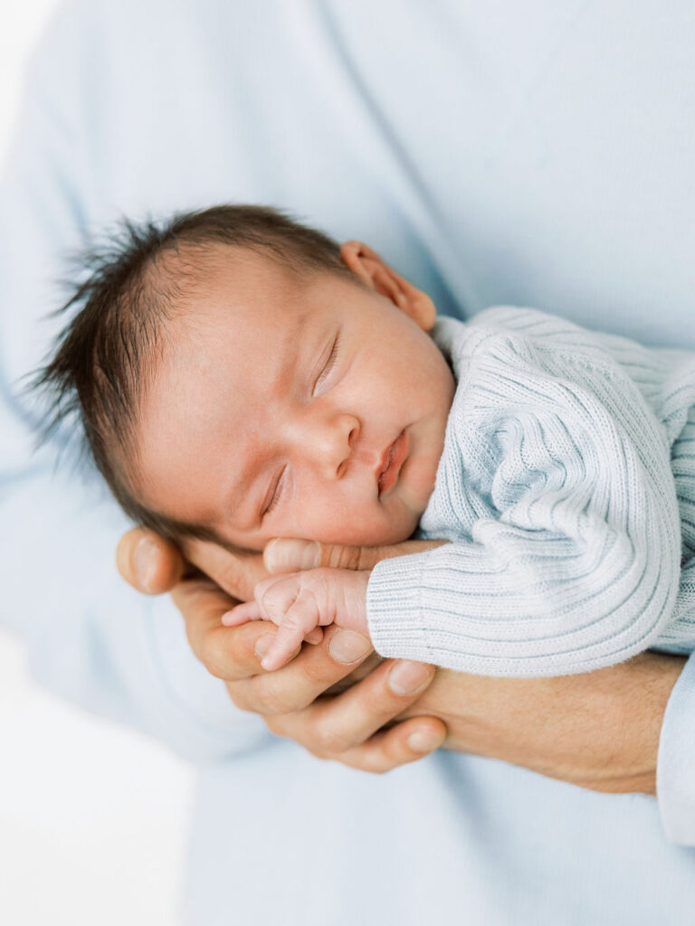 Sleeping newborn baby resting peacefully in a parent’s hands during a studio newborn session