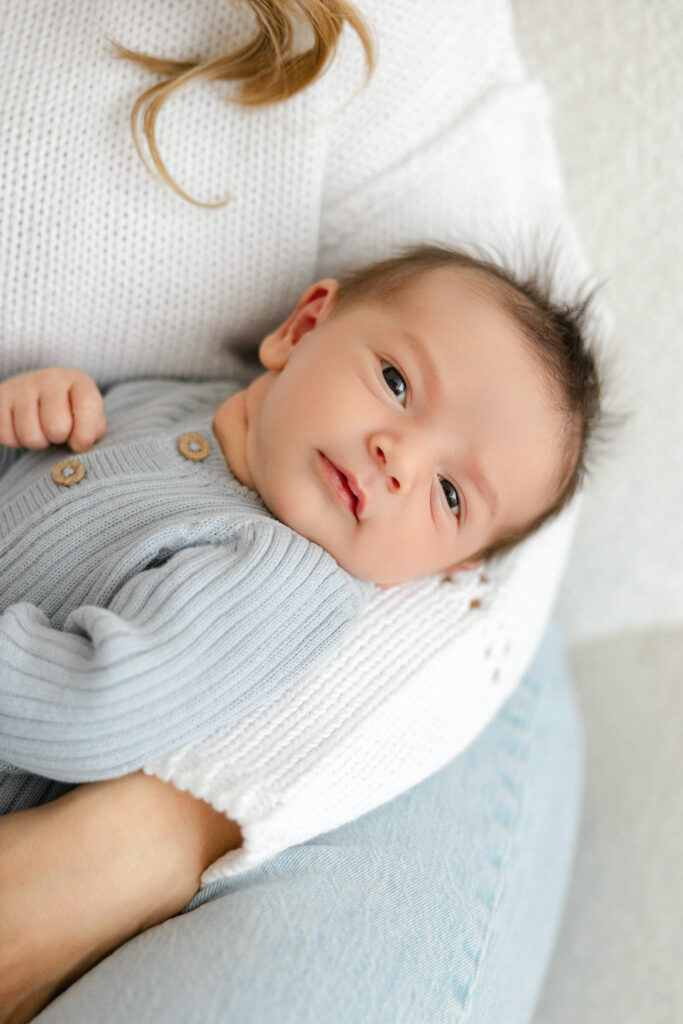 Awake newborn baby resting comfortably in mom’s arms during a natural studio newborn session