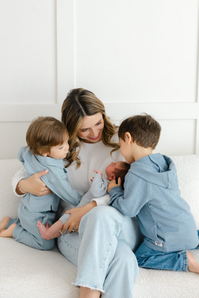 Mom cuddling her newborn baby with two older siblings during a relaxed studio newborn photography session