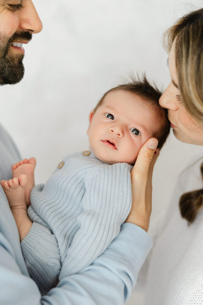 Mom kissing her awake newborn baby while dad looks on during a relaxed studio newborn photography session.