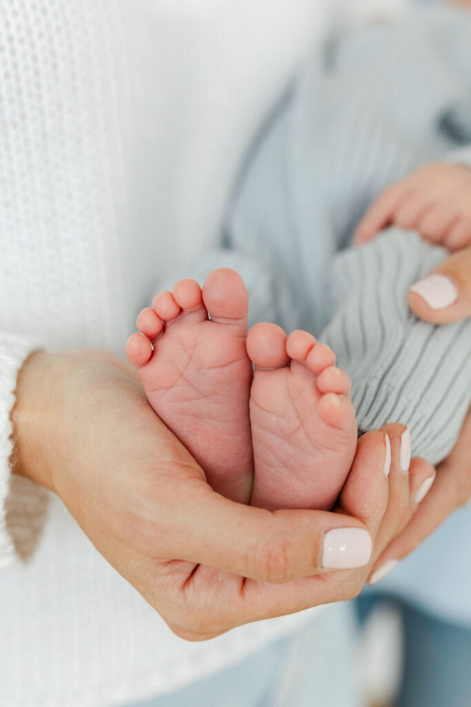 Close up of newborn baby feet gently held in mom’s hands during a natural studio newborn session.