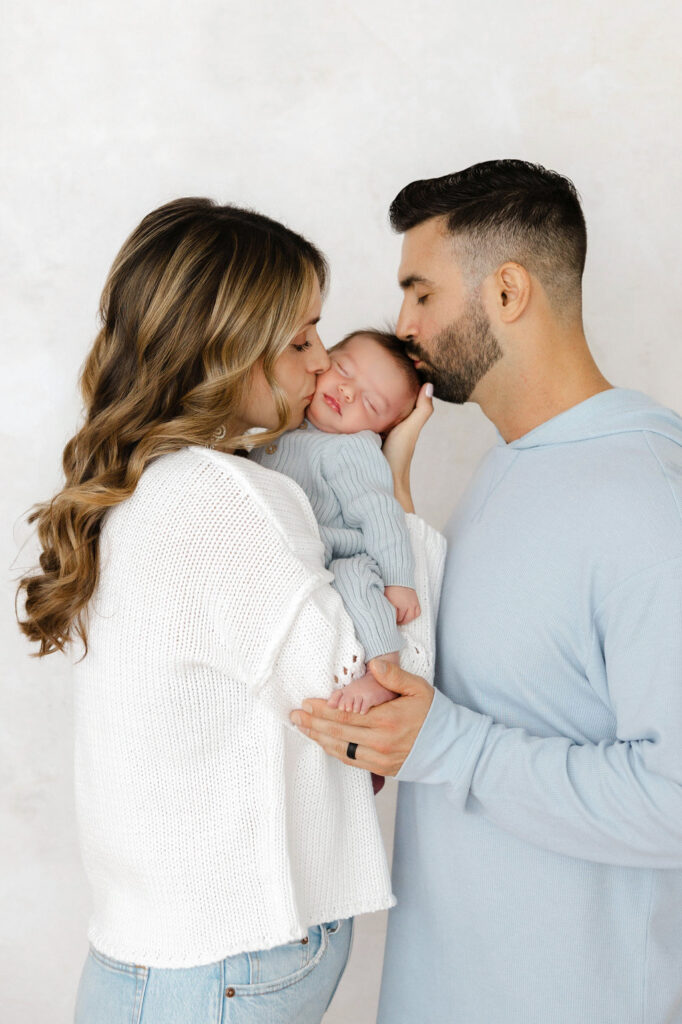 Mom and dad kissing their newborn baby during a studio newborn photography session