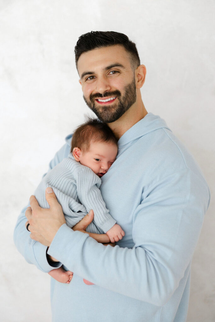 Dad smiling while holding his newborn baby during a studio newborn photography session