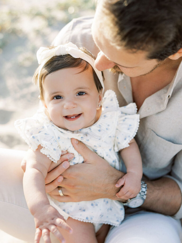 Dad holding his smiling baby girl in a soft floral outfit, paired with neutral tones for a simple family photo look.