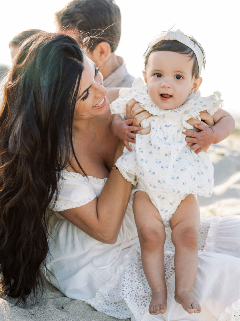 Mom smiling at her baby girl in a soft floral outfit, paired with a simple white dress for a light, coordinated family photo look.