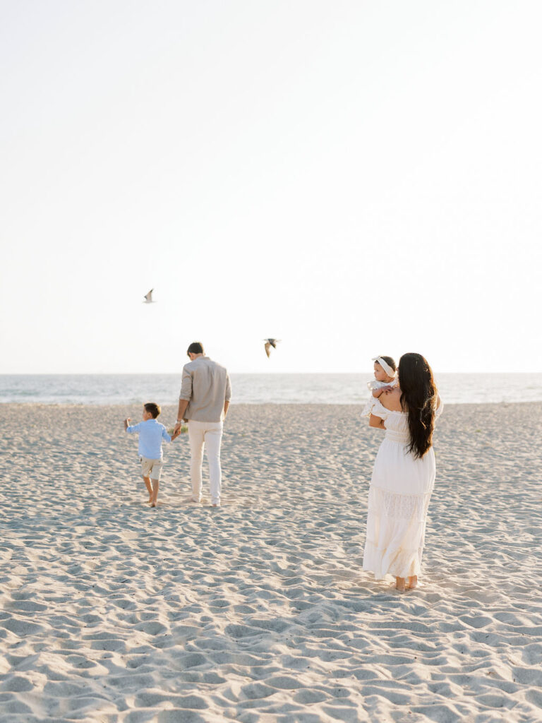 Family walking together on Oxnard Beach with mom holding the baby and dad walking with their son.