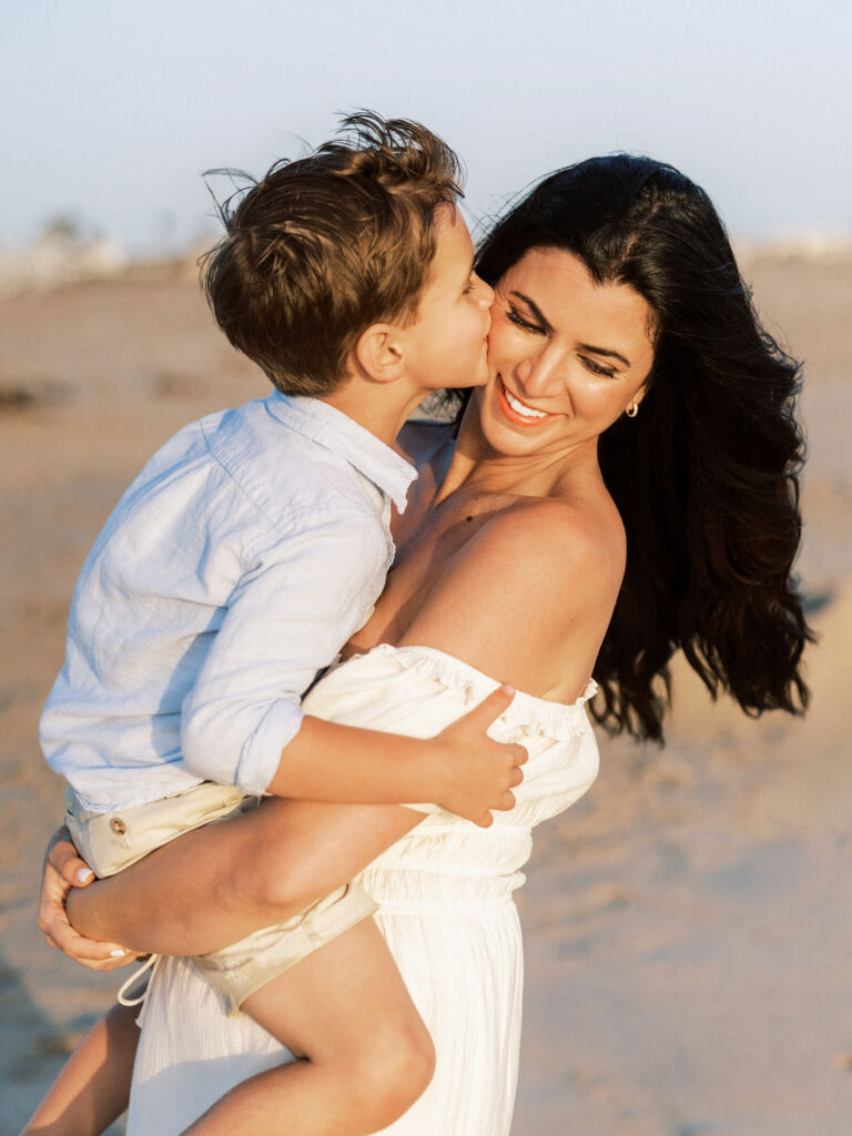 Mom in a white dress holding her son in light blue during a Ventura beach family session