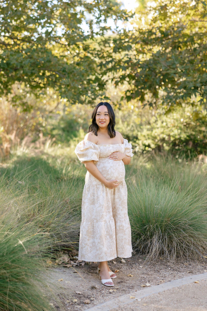 Expecting mom wearing a light floral maternity dress in a natural outdoor setting