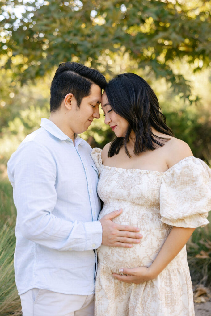 Expecting couple cuddling together in coordinated neutral outfits during their maternity photography session