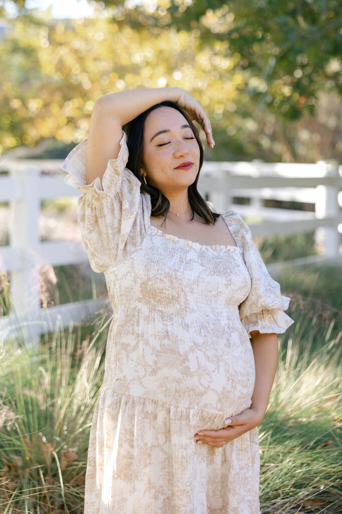 Pregnant mom adjusting her hair while wearing a light floral dress for maternity photos
