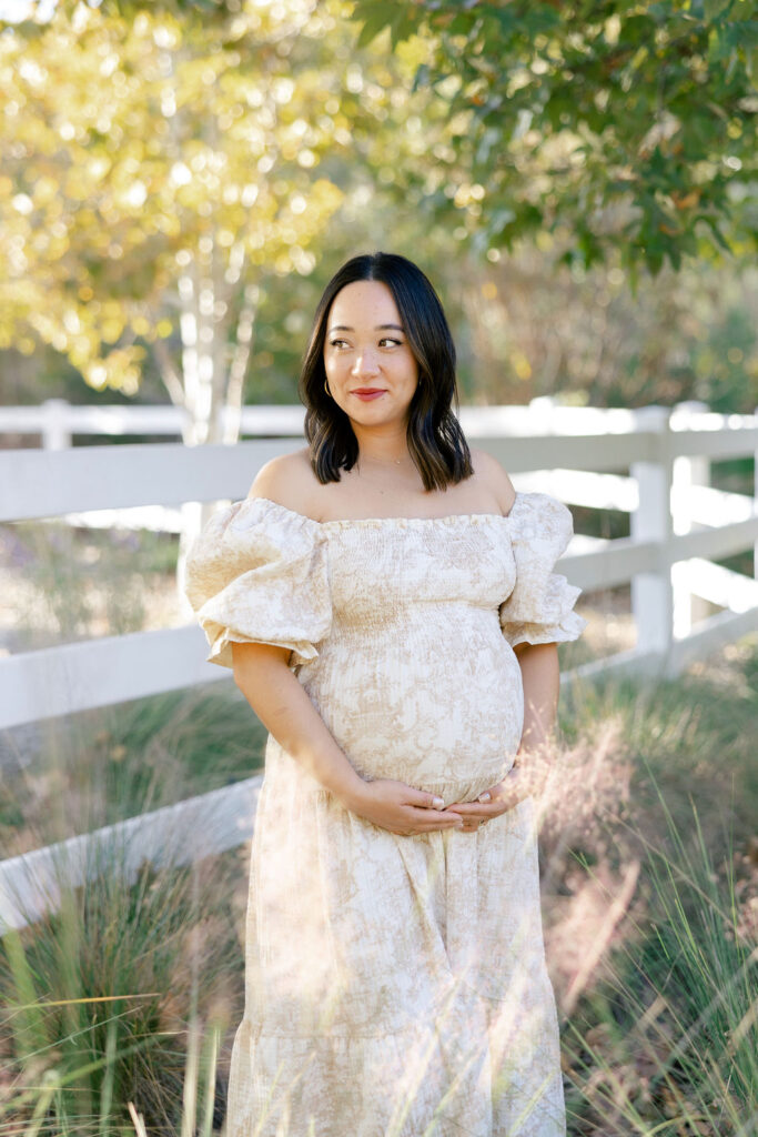 Expecting mom smiling in an off shoulder floral dress during a natural maternity session