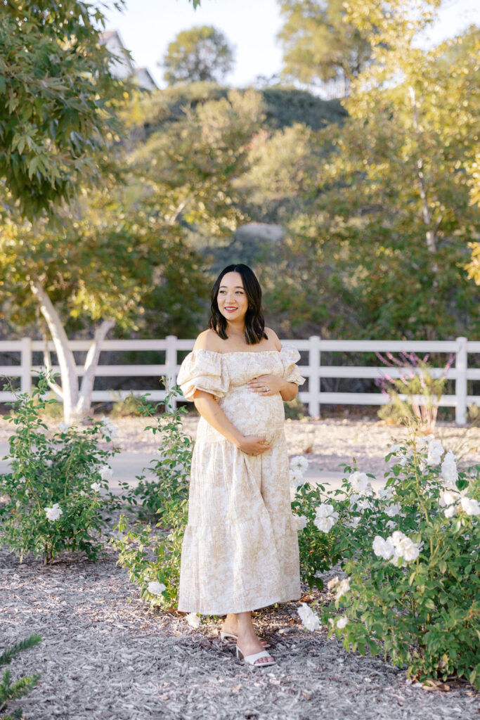 Expecting mom in a flowing floral maternity dress surrounded by soft greenery