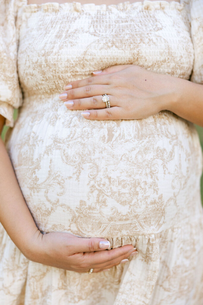 Expecting mom resting her hands on her belly while wearing a feminine floral maternity dress