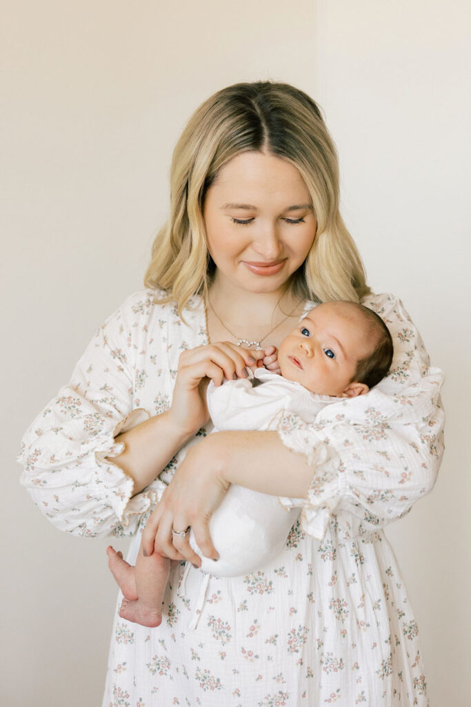 Mom holding her newborn in a soft floral dress and neutral baby outfit during a light and airy Santa Clarita newborn photography session