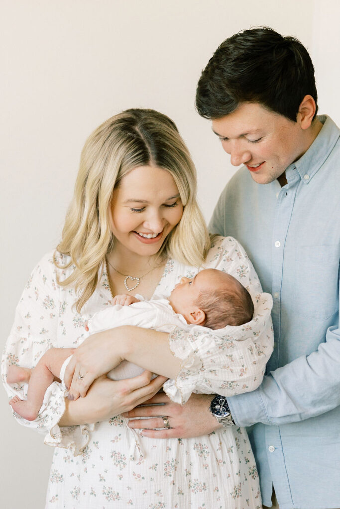 Parents smiling down at their newborn in coordinated soft blue and floral outfits for timeless family photos