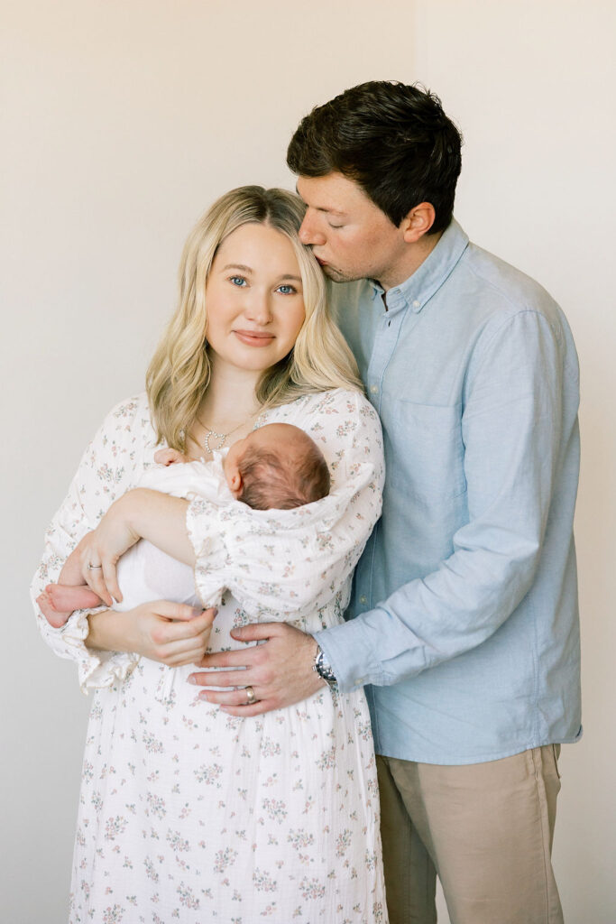 Parents holding their newborn in soft blue and floral outfits, a coordinated neutral look for newborn family photos