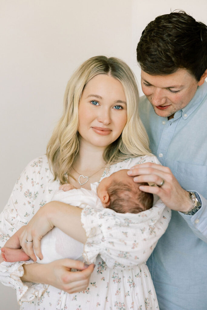 Parents holding their newborn in coordinated soft blue and floral outfits, a simple and timeless choice for newborn family photos