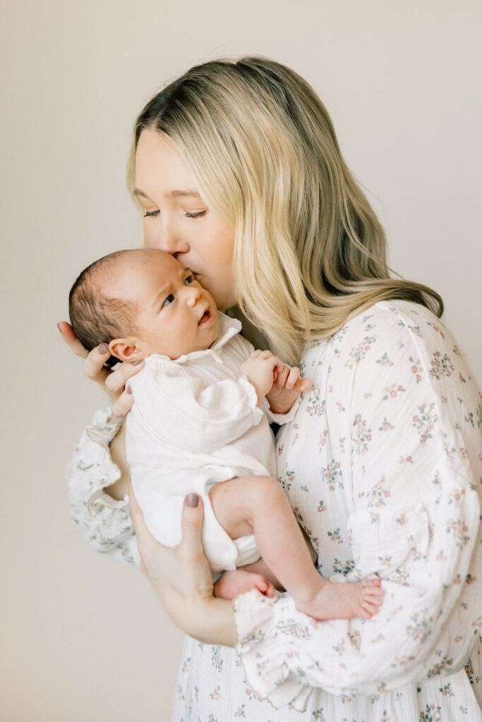 Mom kissing her newborn while wearing a soft floral dress, a timeless look for newborn photos