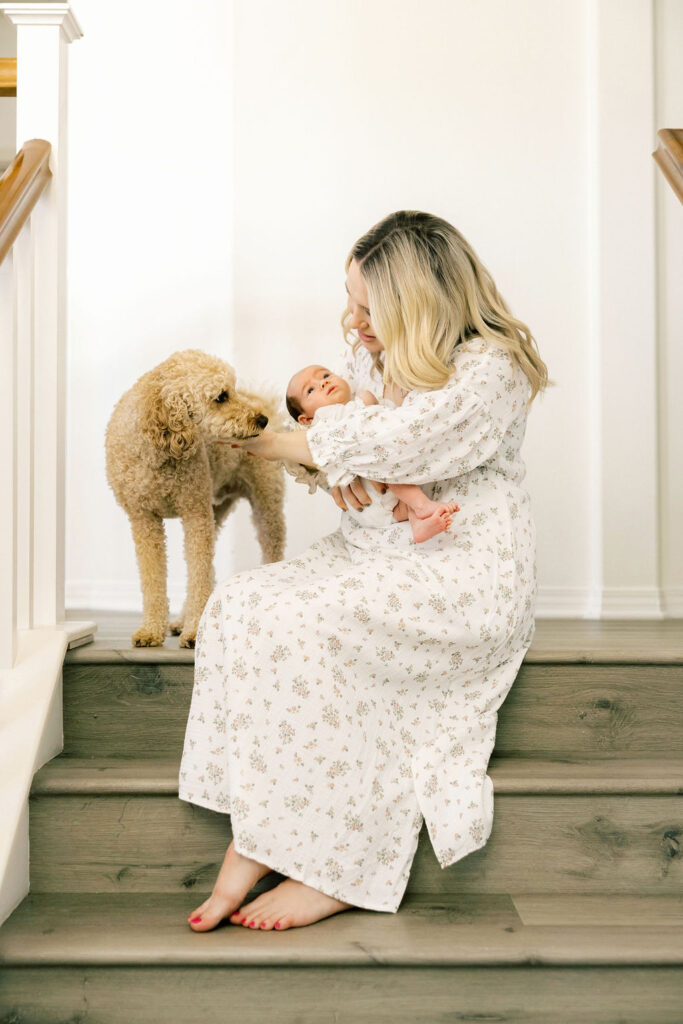 Mom holding her newborn beside the family dog while wearing a soft floral dress, a natural outfit choice for newborn family photos