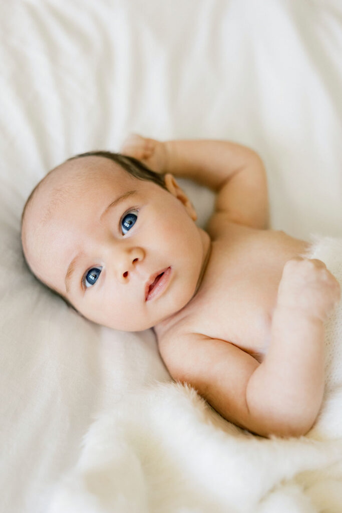 Newborn baby resting on soft white bedding with a simple neutral look for newborn photos