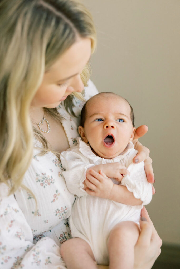 Mom holding her yawning newborn in a white outfit with soft floral tones, offering neutral outfit inspiration for newborn photos in Santa Clarita