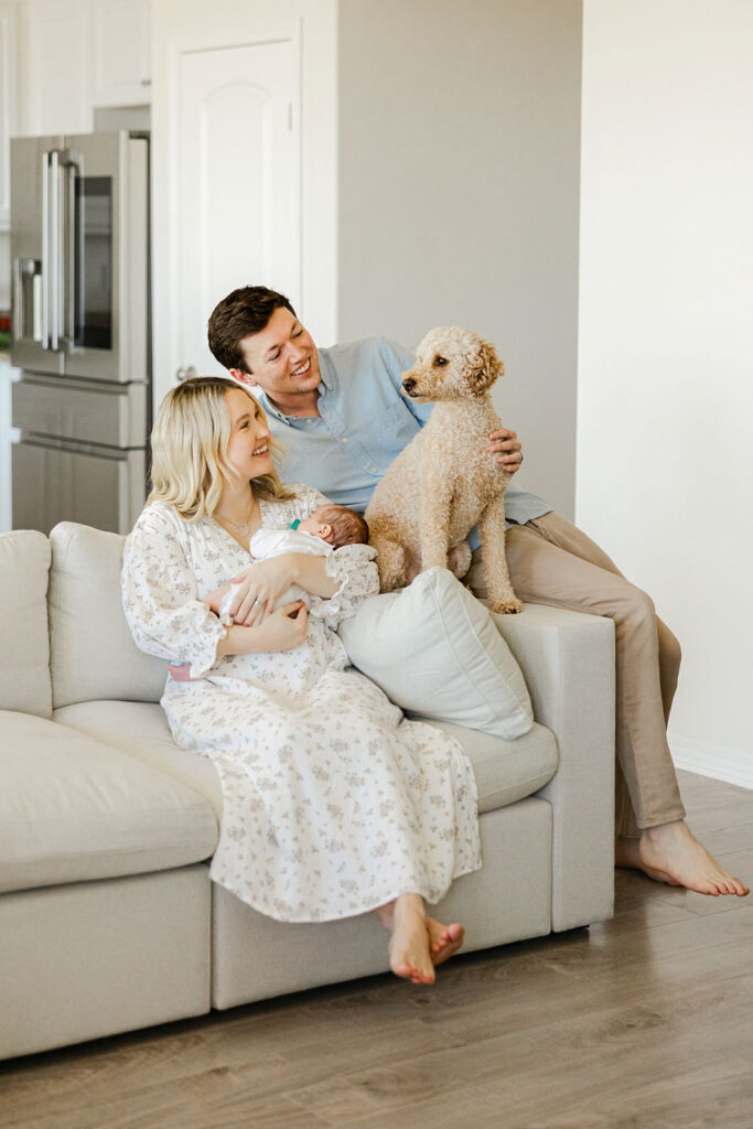 Parents cuddling their newborn with their dog while wearing soft neutral outfits for an in home newborn photography session in Santa Clarita