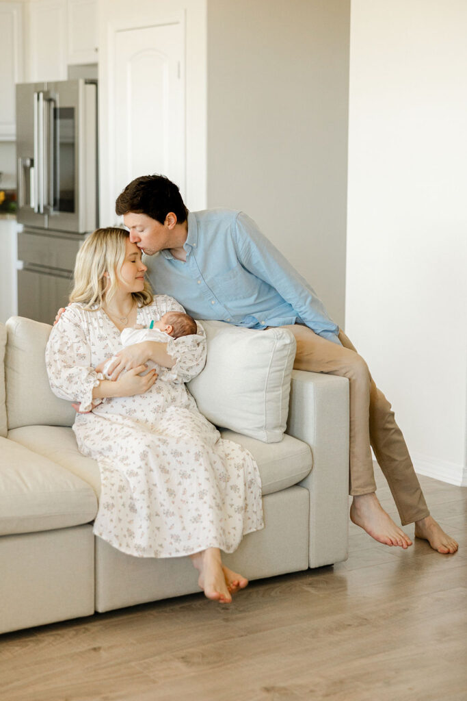 Parents wearing soft neutral and blue outfits while cuddling their newborn during an in home newborn photography session in Santa Clarita