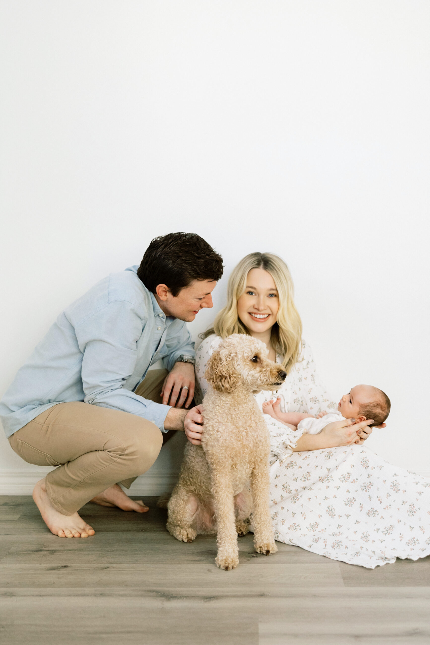 Parents with their newborn and family dog in coordinated soft blue, cream, and floral outfits for relaxed newborn family photos