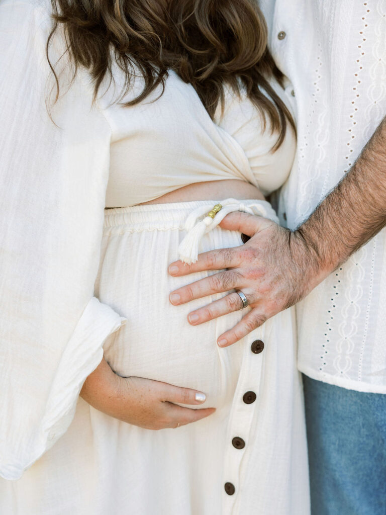 When to Take Maternity Photos with an expecting couple placing their hands on her baby bump during a Santa Clarita maternity session