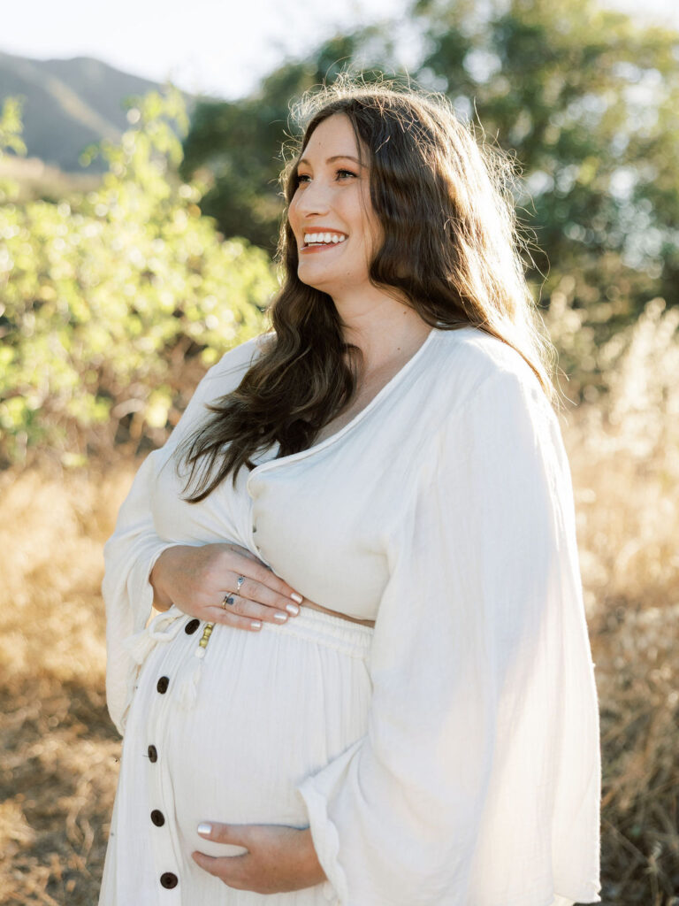 Smiling pregnant woman cradling her baby bump during a golden hour maternity session in Santa Clarita