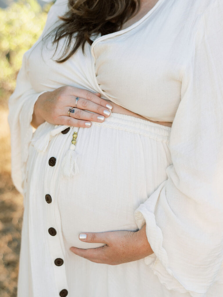 When to Take Maternity Photos with a close up of a pregnant woman gently cradling her baby bump during a Santa Clarita maternity session