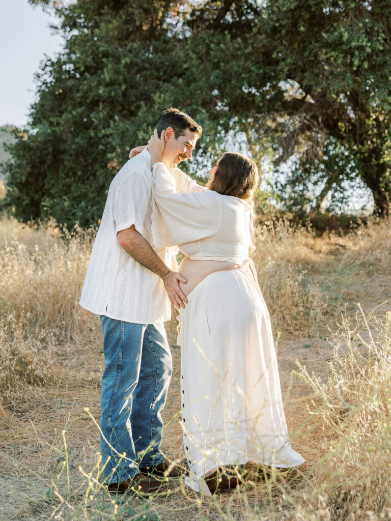 Expecting couple embracing with hands on her baby bump during a golden hour maternity session in Santa Clarita