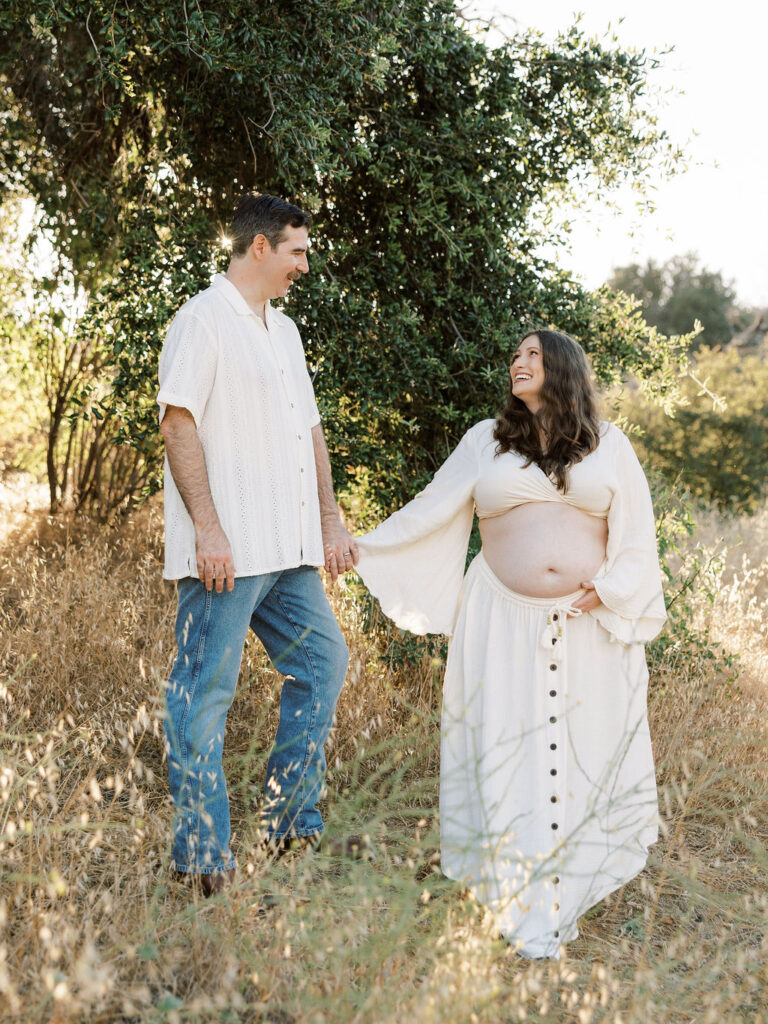 Expecting couple walking hand in hand through a sunlit field during a Santa Clarita maternity session