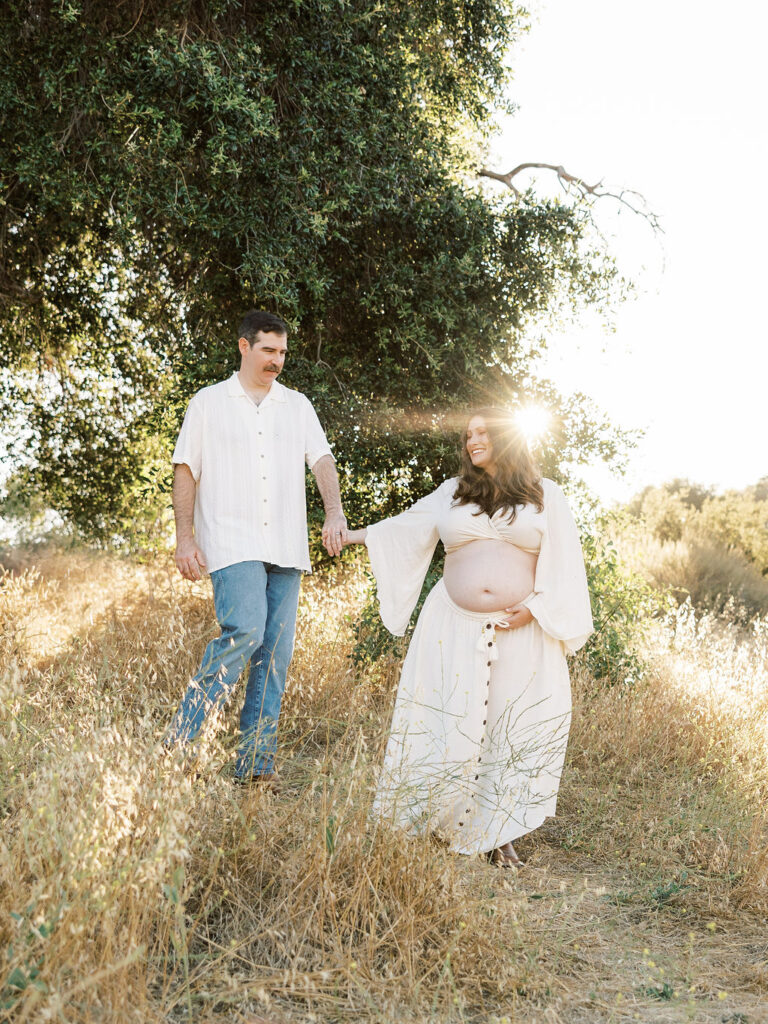 Expecting couple holding hands beneath a tree during a golden hour maternity session in Santa Clarita