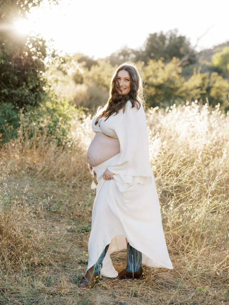 Pregnant woman smiling in a flowing white dress during a golden hour maternity session in Santa Clarita